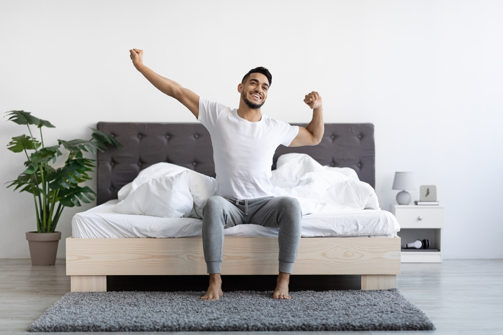 Joyful young man waking up refreshed after chiropractic care, stretching in bed, symbolizing the positive impact of chiropractic on sleep quality.