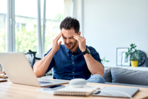 Young man experiencing a headache while working from home, demonstrating the need for chiropractic care
